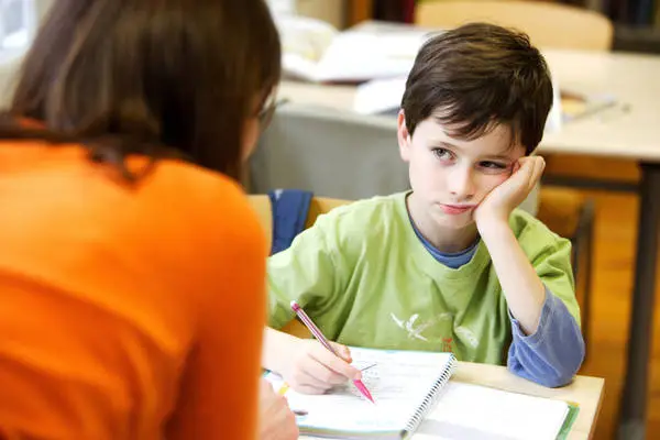 Bambino a scuola con penna e quaderno mentre ascolta distratto l'insegnante