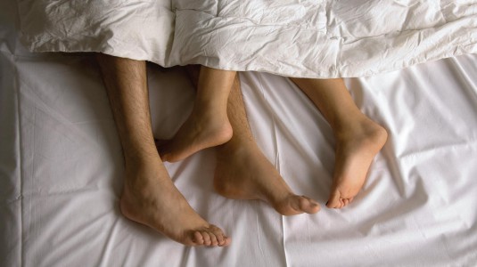piedi nudi di due persone stese nel letto avvolte nelle coperte